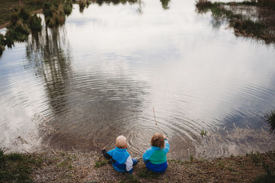 Back view of young kids in front of a lake in a park on cloudy day