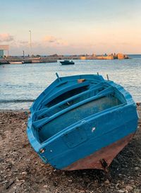 Boat moored on beach against sky during sunset