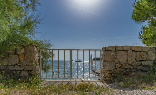 Stone wall by sea against sky on sunny day