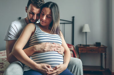 Man embracing pregnant women while sitting on bed at home