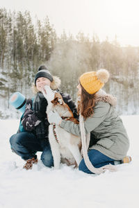 Happy couple with dog on snow covered land against clear sky