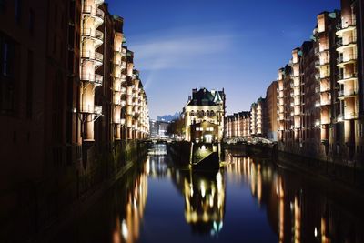 Canal amidst illuminated city against sky