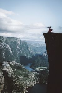 Man sitting on cliff by sea against sky