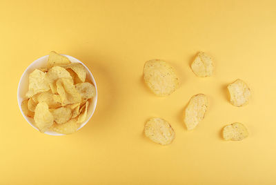 Crispy potato chips in bowl on yellow background, top view