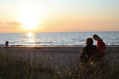 Rear view of people sitting on beach during sunset