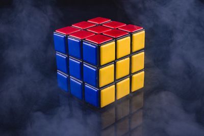 Close-up of multi colored puzzle cube amidst smoke on table against black background