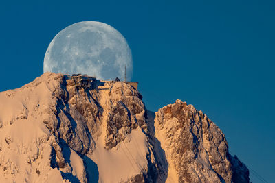 Low angle view of snowcapped mountains against clear blue sky