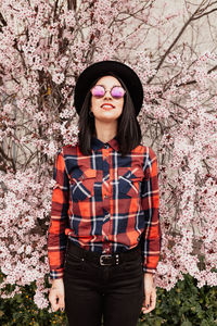 Portrait of smiling woman wearing hat standing by cherry tree