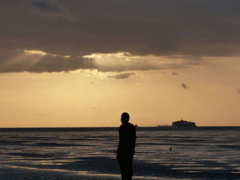 Silhouette man standing on beach against sky during sunset