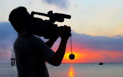 Rear view of man standing against sea during sunset