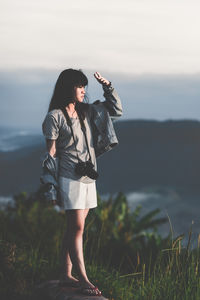 Young woman with digital camera standing against sky