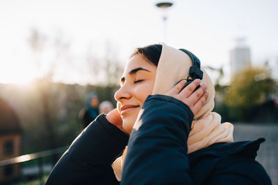 Teenage girl listening to headphones with eyes closed against sky