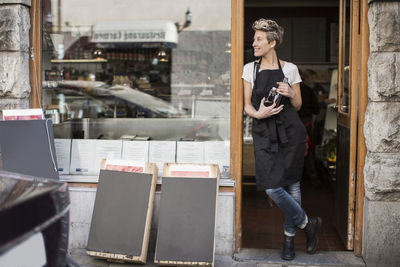 Smiling saleswoman looking away while standing at supermarket entrance