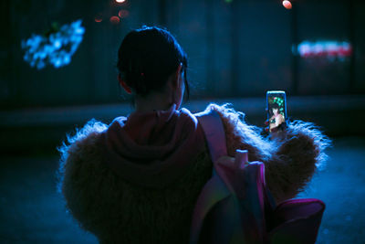 Rear view of woman taking selfie from phone while standing outdoors at night