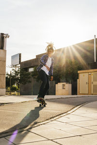 Young man skateboarding on footpath during sunny day