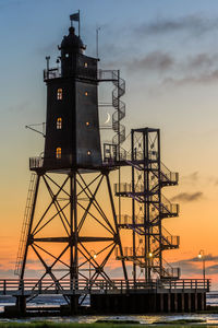 Tower by sea against sky at sunset