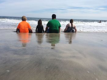 Rear view of family sitting on shore at beach against sky