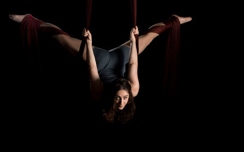 Young woman hanging on fabric while dancing against black background