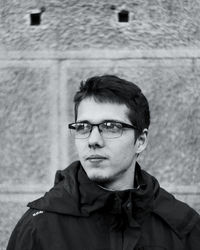 Thoughtful young man wearing eyeglasses looking away against wall