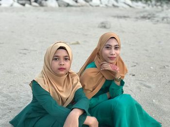 Portrait of female friends in hijab sitting at beach