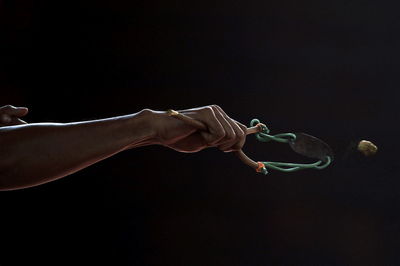 Cropped hand of person holding catapult against black background
