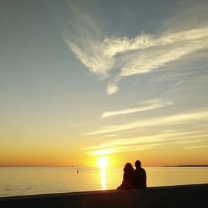 Silhouette men sitting on beach against sky during sunset