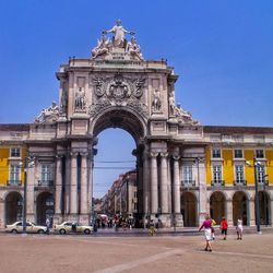 People walking in front of historical building against blue sky