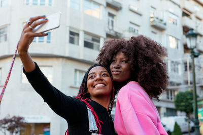 Carefree african american female friends with afro hairstyles taking self portrait on smartphone on street in city