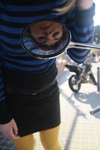 Close-up of woman looking into bike mirror while standing on road 