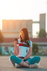 Woman using mobile phone while sitting on road during sunset