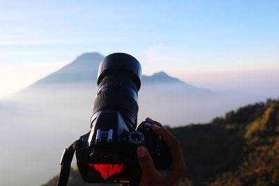 Cropped hand of man photographing against mountains