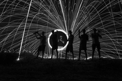 People standing by illuminated fire on field at night