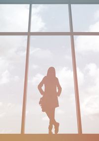 Silhouette woman standing by glass window against cloudy sky