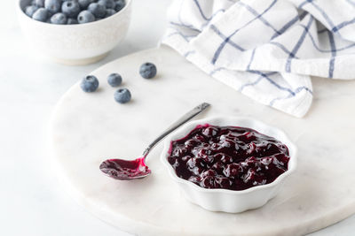 Close up view of a bowl of sweet homemade blueberry sauce on a marble slab.