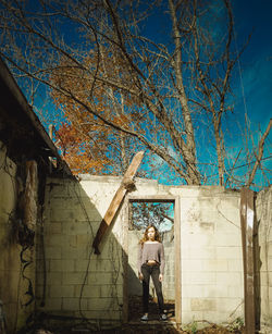 Man standing by bare tree against building