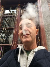 Low angle view of bald man exhaling smoke against window