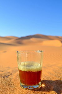 Glass of beer on sand against sky