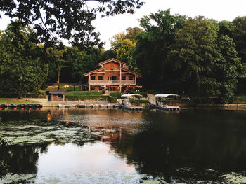 House by lake and buildings against trees