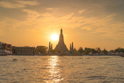 Scenic view of river by buildings against sky during sunset