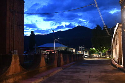 Road by illuminated buildings against sky at dusk