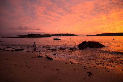 Rear view of man standing at beach against sky during sunset