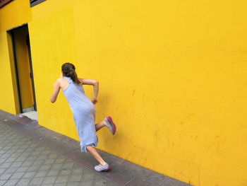 Full length of woman standing against yellow wall