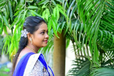 Smiling young woman standing by leaves on tree