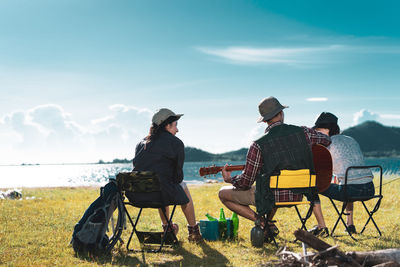 Rear view of people sitting on bench against sky