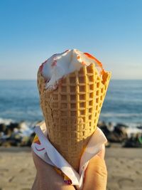 Cropped hand holding ice cream cone at beach