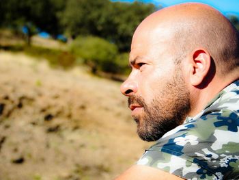 Profile view of thoughtful bald man with beard against trees