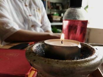 Midsection of person with tea light candle on table