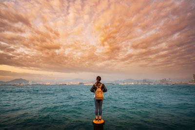 Man standing in sea against sky during sunset