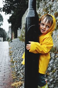 Boy looking away while standing by pole on street