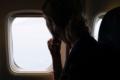 Side view of woman looking through airplane window